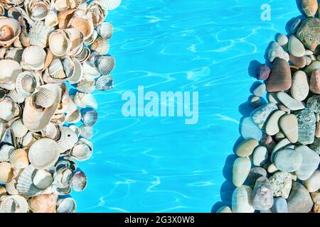 Summer background pattern from seashells and sea pebbles in blue water with copy space. Stock Photo
