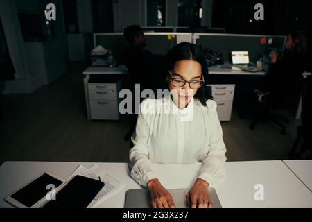 Young businesswoman working on laptop at desk with colleagues in the background Stock Photo