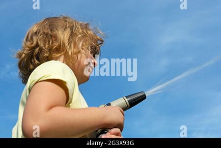 Child with water gun and water jet in front of blue sky Stock Photo