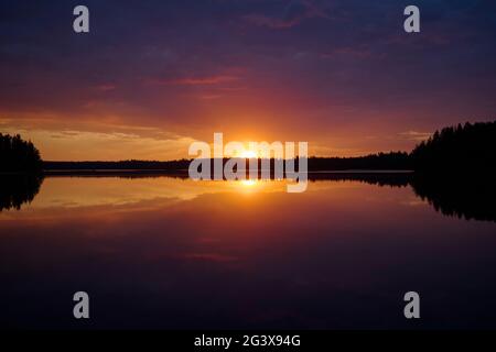 Scenic and beautiful sunset and colorful cloudy sky and their reflections on a lake in Finland at summer. Stock Photo