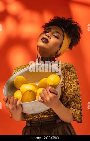 african american woman posing with metal bowl with lemons on orange Stock Photo