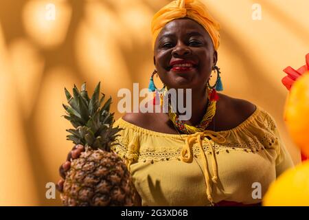smiling middle aged african american woman holding pineapple in hand on orange Stock Photo