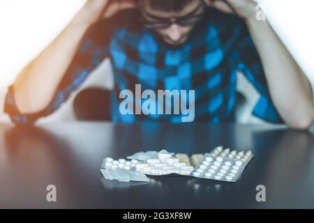 Depressed man taking drugs. Young man sitting on a table, drugs and pills in front of him Stock Photo