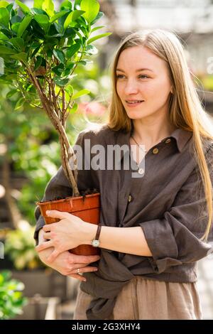 Portrait of a pretty woman worker of garden center with a potted plant in her hands Stock Photo