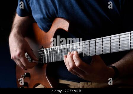 Close up of a man playing a guitar. Dark background, blue shirt and selective focus. Stock Photo