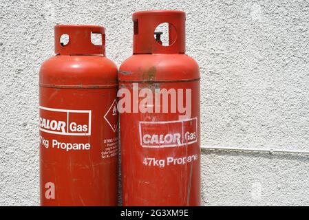 Two large red 47kg Calor gas canisters / propane against a white wall Stock Photo