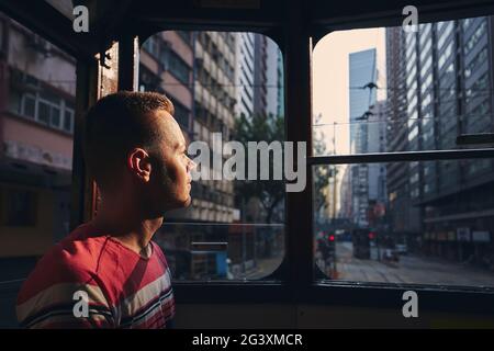 Pensive man looking out old tram window. Tourist exploring  city streets of Hong Kong. Stock Photo