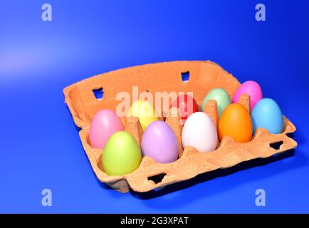 Easter eggs in a paperboard. Multi-colored eggs in egg carton on blue background. Easter is a Christian holiday that celebrates the belief in the resu Stock Photo