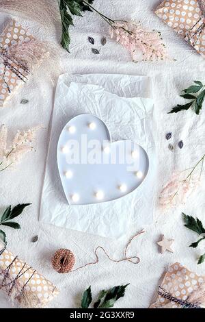 Heart lightbox. Background with wild flowers and natural materials. Flat lay on off white textile with white wrapping paper, gift boxes wrapped in Stock Photo