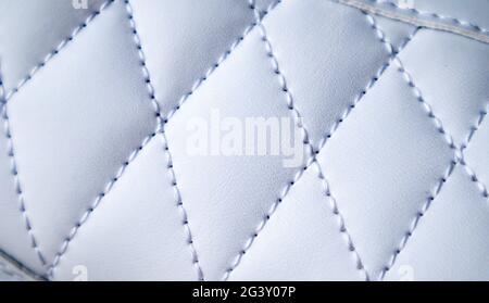 Close-up of synthetic fabric with white diamond stitching. Texture the diamond in a classic style. Luxurious background. Quilted fabric in white or li Stock Photo