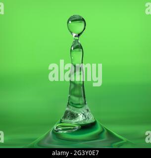 Water droplet landing in water on a green background Stock Photo