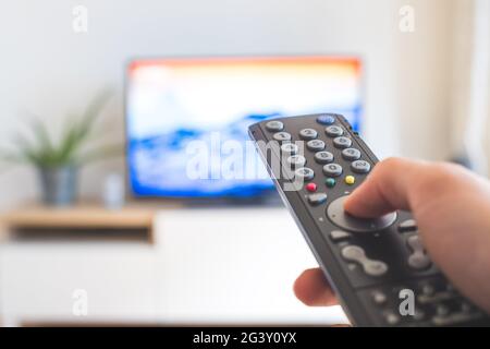 Male hand is holding TV remote control, streaming on a smart TV. Stock Photo