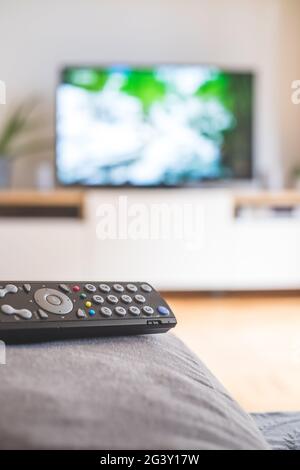 Remote control on the sofa, streaming on a smart TV. Stock Photo