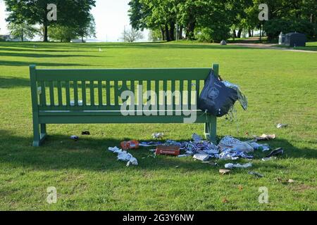 Litter and mess left by a park bench, two trash cans nearby on the background. Kaivopuisto Park, Helsinki, Finland. June 6, 2021. Stock Photo