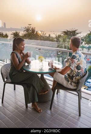 Couple mid age having breakfast on balcony in Thailand Pattaya looking out over the ocean, men and woman European and Asian woma Stock Photo