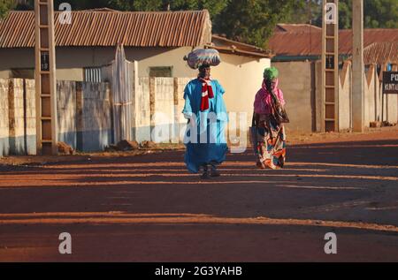 Gambia; Central River Region; Main street of Kuntaur; Married couple with luggage on their heads; Street scene in the morning sun; Stock Photo