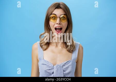 Waist-up shot of excited surprised and emotive charismatic caucasian woman in trendy sunglasses opening mouth from amazement and Stock Photo