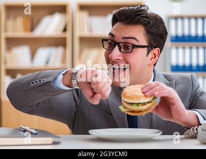 Hungry funny businessman eating junk food sandwich Stock Photo