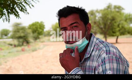 Handsome Indian man wearing mask and check shirt over blur background with serious face. Stock Photo