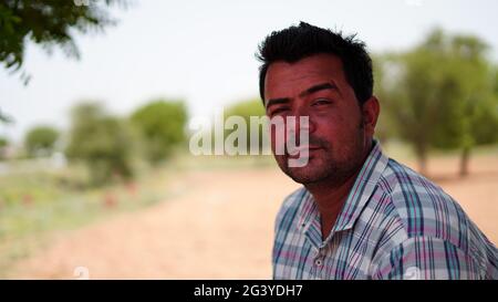Side view of charming Indian man looking at camera while sitting against blurred outdoor background Stock Photo