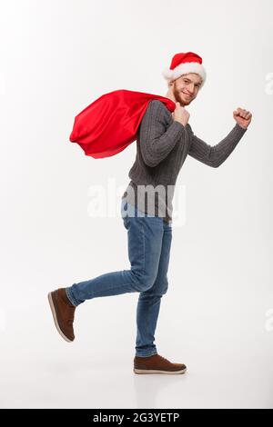 Christmas concept - Young confident beard man running and holding red big santa bag with a lot of present inside. Stock Photo