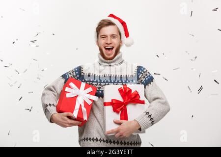 Chirstmas Concept - Happy young caucasian beard man holding present box with confetti background celebrating for Christmas day. Stock Photo