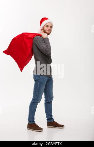 Christmas concept - Young confident smart man holding red big santa bag with a lot of present inside. Stock Photo