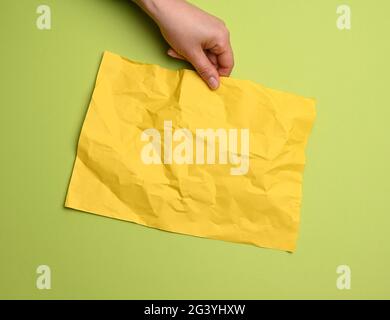 Female hand holding blank crumpled yellow sheet of paper on a green background Stock Photo