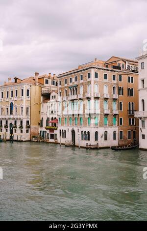 A gondola with tourists is sailing along the Grand Canal amid the facades of Venetian houses standing on the water in Venice, It Stock Photo
