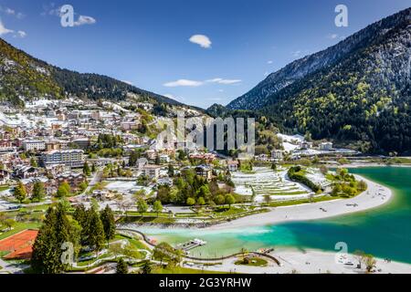 The Improbable aerial landscape of village Molveno, Italy, azure water of lake, empty beach, snow covered mountains Dolomites on Stock Photo