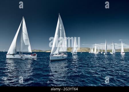 Sailboats compete in a sail regatta at sunset, race of sailboats, reflection of sails on water, multicolored spinnakers, number Stock Photo