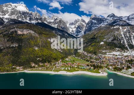 The Improbable aerial landscape of village Molveno, Italy, azure water of lake, empty beach, snow covered mountains Dolomites on Stock Photo