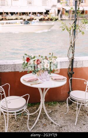 A white table and chairs for two, in a restaurant on the banks of the Grand Canal in Venice, Italy. On the table there is a larg Stock Photo