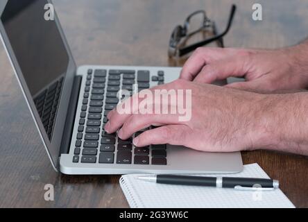 side view close-up of person working on laptop computer at wooden desk Stock Photo