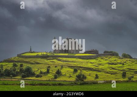 Rock of Cashel castle on green hill illuminated by sunlight with storm clouds in background Stock Photo