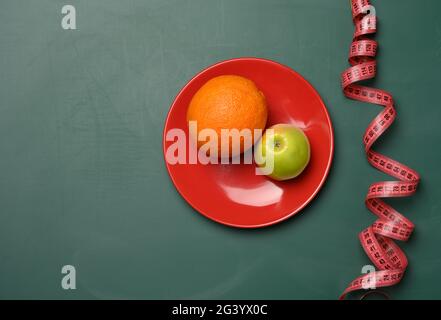Green apple and red round plate, red measuring tape on a green background Stock Photo