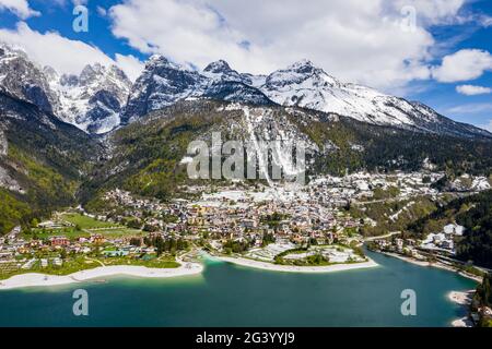 The Improbable aerial landscape of village Molveno, Italy, azure water of lake, empty beach, snow covered mountains Dolomites on Stock Photo
