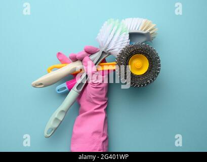 Female hand in a pink glove holds a stack of plastic cleaning brushes Stock Photo