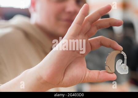 A young man puts on a hearing aid. Portable sound amplifier for the deaf and hearing impaired Stock Photo