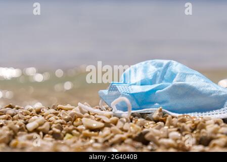 Used blue medical face mask lies on the beach. Environmental and coast plastic pollution during covid-19 pandemics Stock Photo