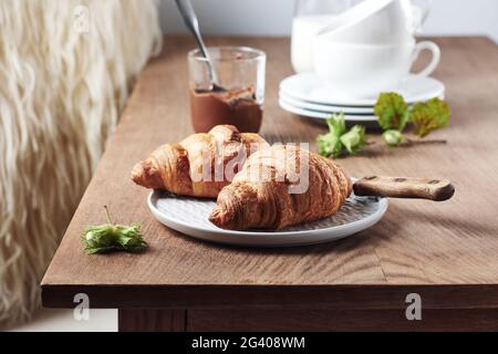 Two croissants with chocolate cream and hazelnuts on a wooden table. Stock Photo