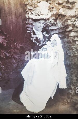 Early 20th century authentic vintage photograph of mother holding baby sitting in garden. Concept of nurturing, caring, love, togetherness, nostalgia Stock Photo