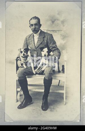 Authentic vintage photograph of senior adult man sitting on chair holding two dogs. Concept of togetherness, friendship, mans best friend Stock Photo