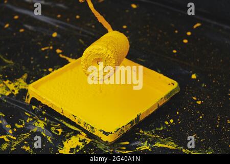 Paint roller with melting yellow paint in a paint tray. Apartment renovation. Black plastic background. Trendy color. Horizontal photo. Stock Photo