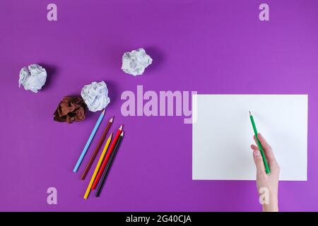Woman going to draw with colored pencils on a purple background with crumpled paper balls. Top view