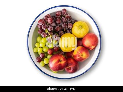 top view of white enamel bowl with blue rim filled with fresh fruits isolated on white background Stock Photo