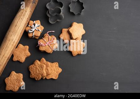 Baked star shaped gingerbread cookies, wooden rolling pin and metal cutters on a black table Stock Photo
