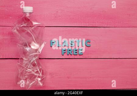 Plastic free concept. Crumpled bottle on red wooden background with text plastic free Stock Photo