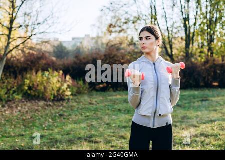 Attractive brunette engaged in dumbbells outdoors. Stock Photo