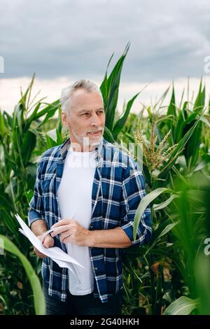 Concentrated farmer on a corn field. A man with important papers in his hands is working outdoors. Stock Photo